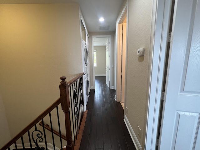 hallway with dark wood-type flooring, an upstairs landing, baseboards, stacked washing maching and dryer, and attic access