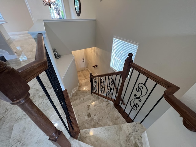 staircase featuring marble finish floor and an inviting chandelier