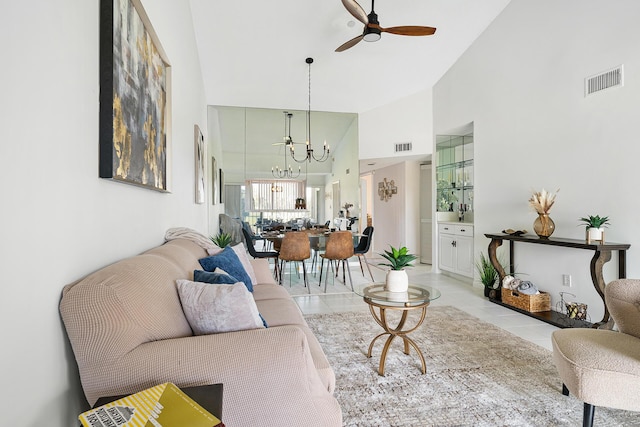 living area with light tile patterned floors, a high ceiling, visible vents, and ceiling fan with notable chandelier