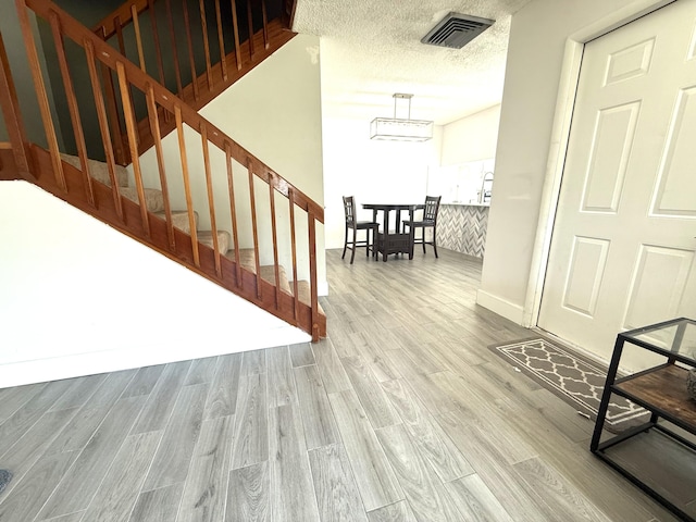 staircase featuring wood finished floors, visible vents, and a textured ceiling