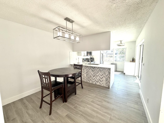 dining area with baseboards, light wood finished floors, and a textured ceiling