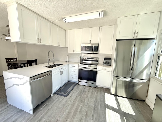 kitchen featuring light wood finished floors, light countertops, stainless steel appliances, white cabinetry, and a sink