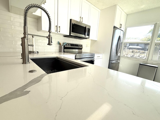 kitchen with backsplash, appliances with stainless steel finishes, white cabinets, and a textured ceiling