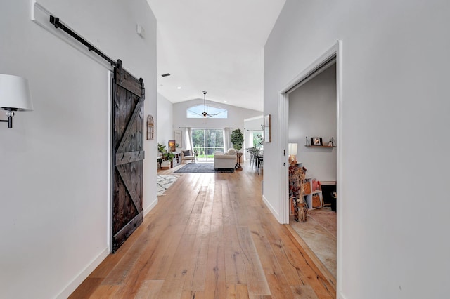 hall featuring light wood-type flooring, a barn door, baseboards, and vaulted ceiling