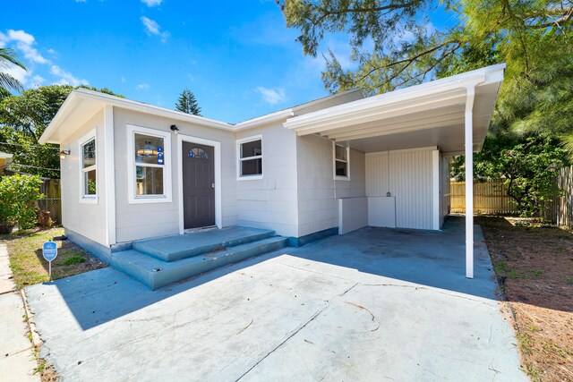 view of front of house with concrete driveway, an attached carport, and fence