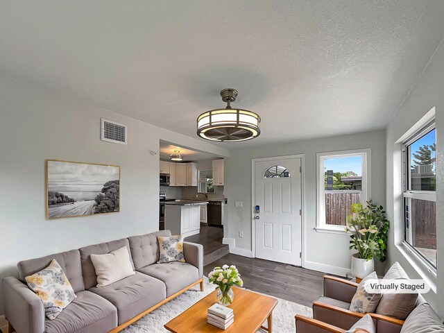 living room with dark wood-style floors, baseboards, visible vents, and a textured ceiling