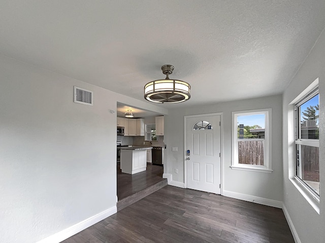 unfurnished dining area featuring baseboards, visible vents, dark wood finished floors, and a textured ceiling