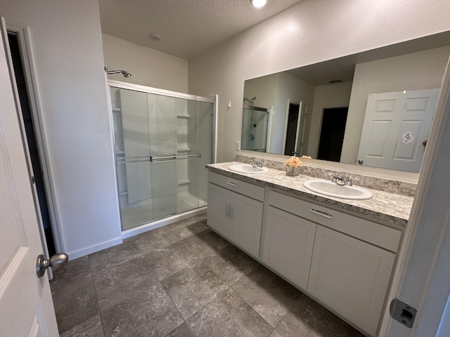 full bath with double vanity, a sink, a shower stall, and a textured ceiling