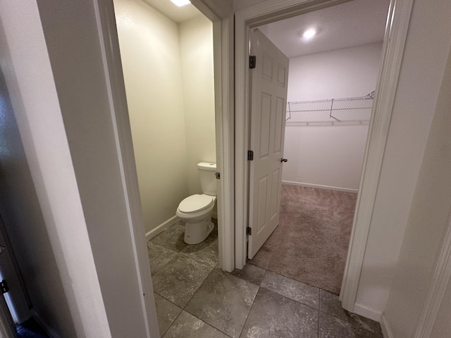 bathroom featuring a walk in closet, toilet, and baseboards