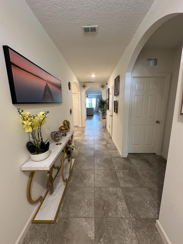 hallway featuring arched walkways, visible vents, and baseboards