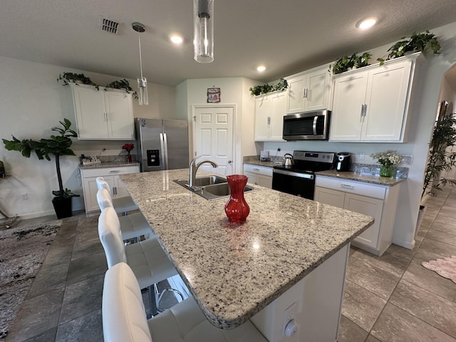 kitchen with light stone counters, a center island with sink, visible vents, appliances with stainless steel finishes, and a sink