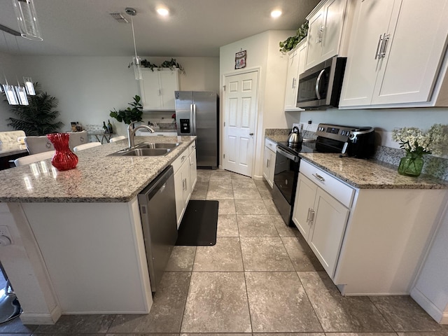 kitchen featuring light stone counters, stainless steel appliances, white cabinets, a sink, and an island with sink