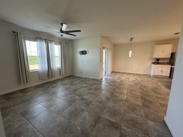 unfurnished living room with a textured ceiling, ceiling fan, and baseboards