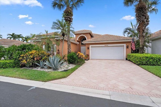 mediterranean / spanish house featuring an attached garage, a tile roof, decorative driveway, and stucco siding