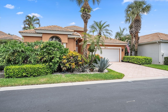 mediterranean / spanish-style home with a garage, driveway, a tile roof, and stucco siding