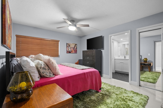 tiled bedroom with a textured ceiling, ensuite bath, a ceiling fan, and baseboards