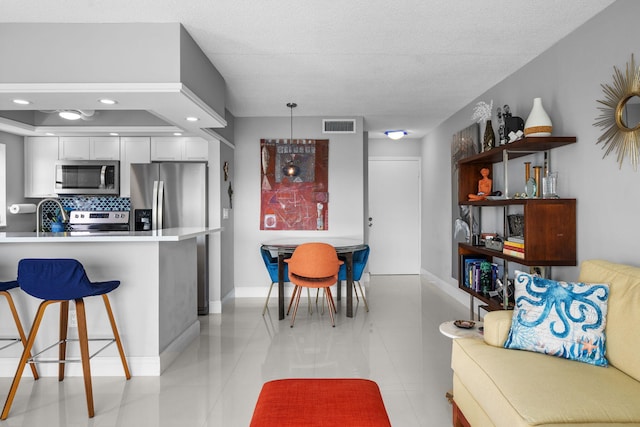 kitchen with a breakfast bar, visible vents, white cabinetry, appliances with stainless steel finishes, and tasteful backsplash