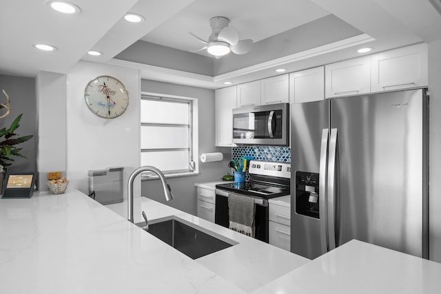 kitchen featuring a sink, white cabinets, appliances with stainless steel finishes, a tray ceiling, and tasteful backsplash