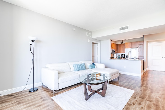 living area featuring baseboards, visible vents, and light wood finished floors