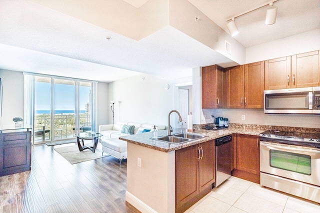 kitchen featuring a peninsula, a sink, open floor plan, appliances with stainless steel finishes, and brown cabinets