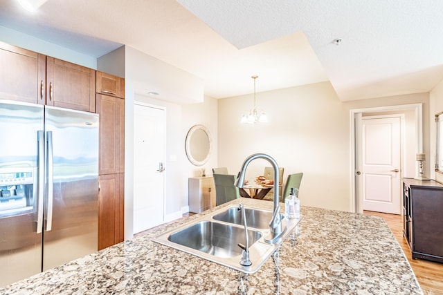 kitchen with a sink, decorative light fixtures, stainless steel fridge, an inviting chandelier, and light wood finished floors