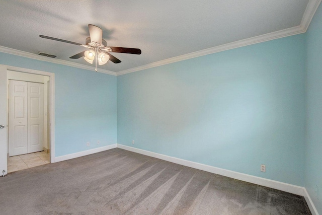 carpeted spare room featuring a ceiling fan, visible vents, crown molding, and baseboards