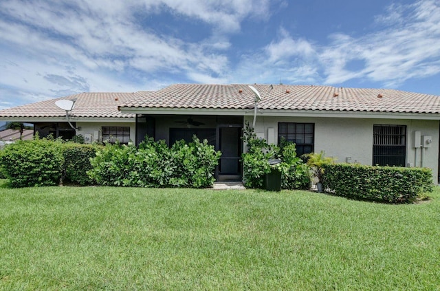 rear view of property featuring a tiled roof, a lawn, and stucco siding