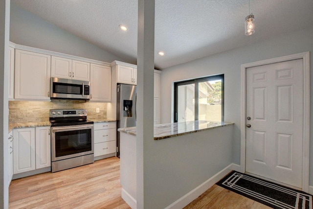 kitchen with lofted ceiling, stainless steel appliances, white cabinetry, light wood-style floors, and decorative backsplash