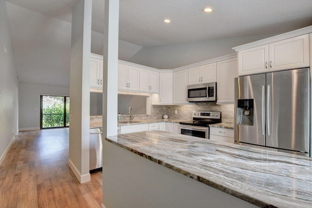 kitchen featuring light stone counters, stainless steel appliances, lofted ceiling, tasteful backsplash, and white cabinetry