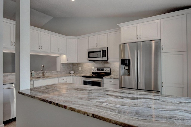 kitchen with lofted ceiling, stainless steel appliances, a sink, and white cabinetry