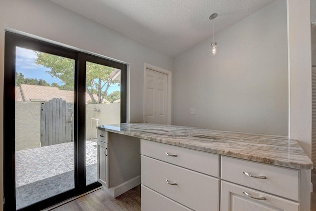 kitchen featuring lofted ceiling, white cabinetry, light stone countertops, light wood finished floors, and decorative light fixtures