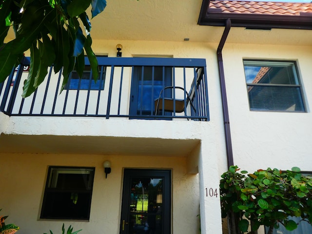 doorway to property with a balcony, a tiled roof, and stucco siding