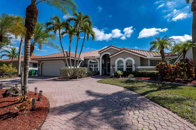 mediterranean / spanish-style home with stucco siding, a tiled roof, an attached garage, decorative driveway, and a front yard