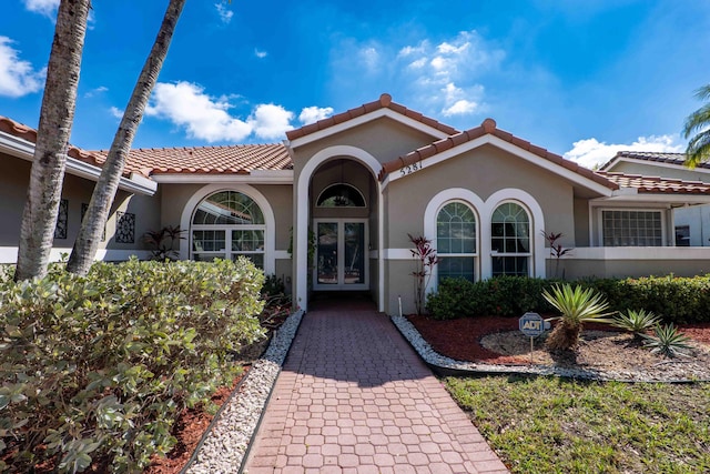 view of exterior entry with french doors, a tiled roof, and stucco siding