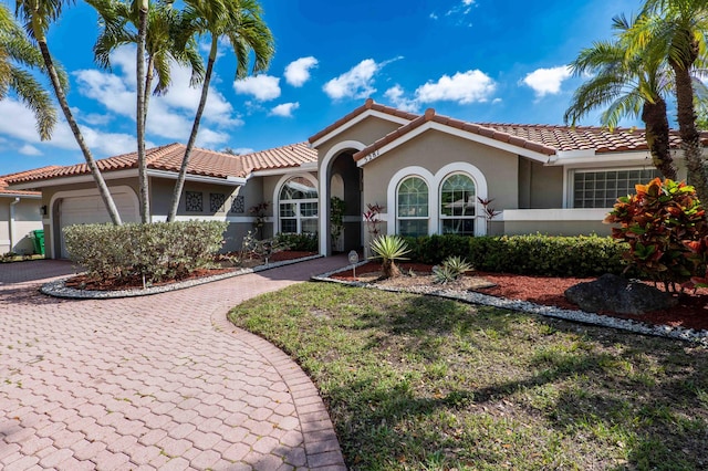 mediterranean / spanish house featuring an attached garage, a tiled roof, decorative driveway, and stucco siding