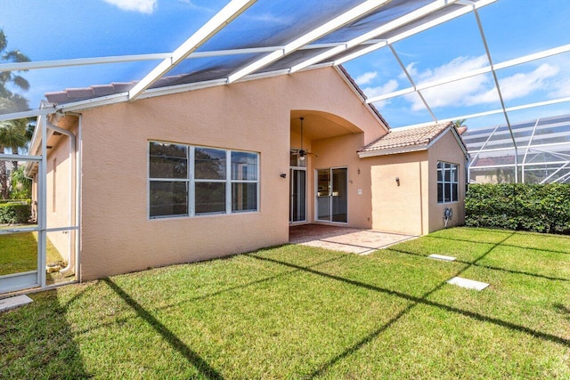 rear view of property with a patio, a lanai, a tile roof, a yard, and stucco siding