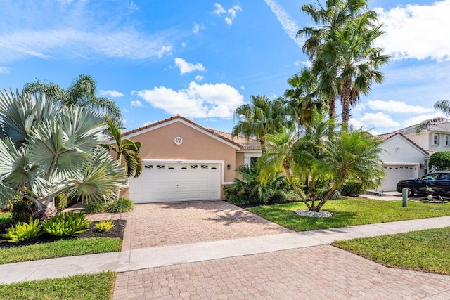 mediterranean / spanish home featuring stucco siding, a tile roof, an attached garage, decorative driveway, and a front yard