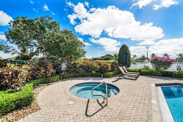 community pool with a patio area, fence, and a hot tub