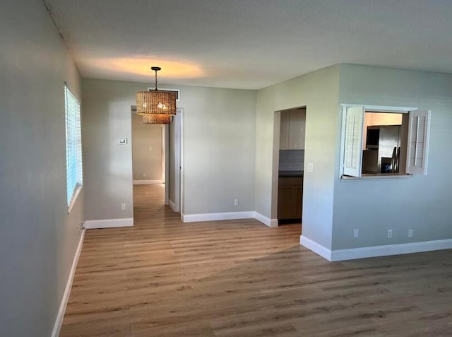 spare room with a notable chandelier, baseboards, and wood finished floors