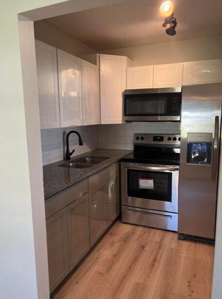 kitchen with appliances with stainless steel finishes, light wood-type flooring, a sink, and white cabinets