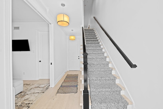 staircase featuring visible vents, crown molding, baseboards, and wood finished floors