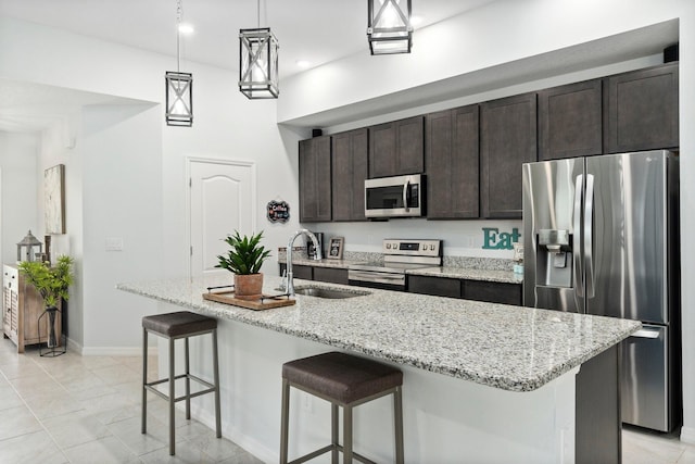 kitchen with dark brown cabinetry, stainless steel appliances, a sink, an island with sink, and a kitchen bar