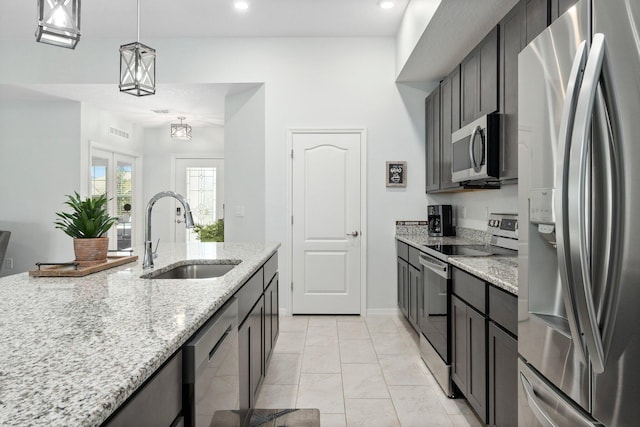 kitchen featuring appliances with stainless steel finishes, light stone counters, a sink, and decorative light fixtures