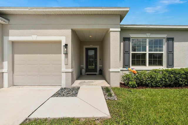 view of exterior entry with driveway, an attached garage, and stucco siding