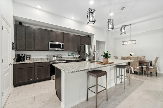 kitchen with dark brown cabinetry, an island with sink, a breakfast bar area, stainless steel appliances, and pendant lighting