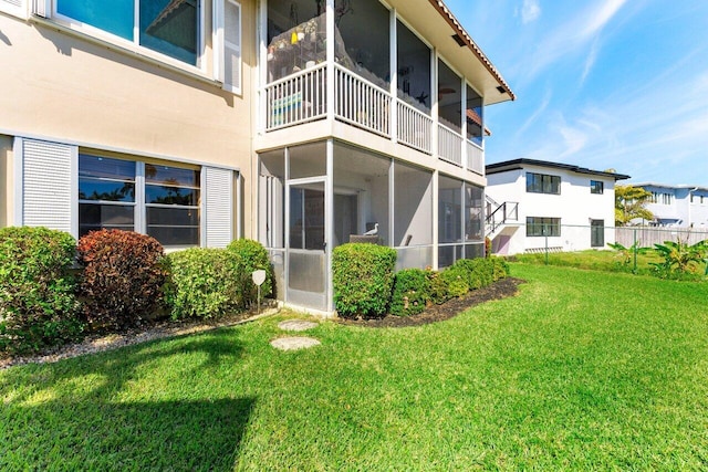 rear view of house featuring a yard, fence, a sunroom, and stucco siding