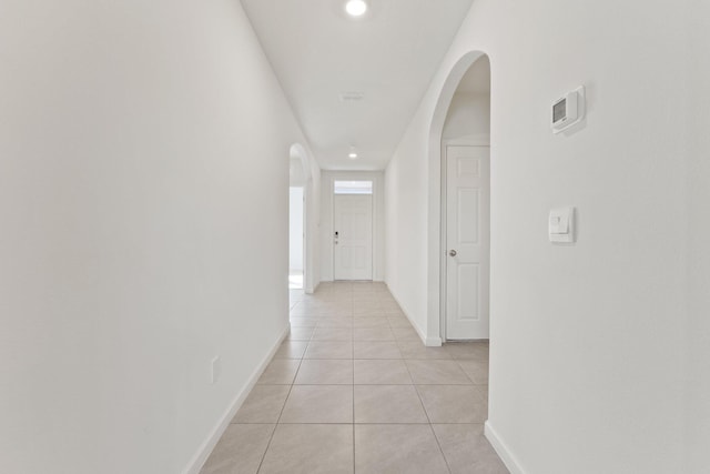 hallway with light tile patterned floors, baseboards, arched walkways, and recessed lighting