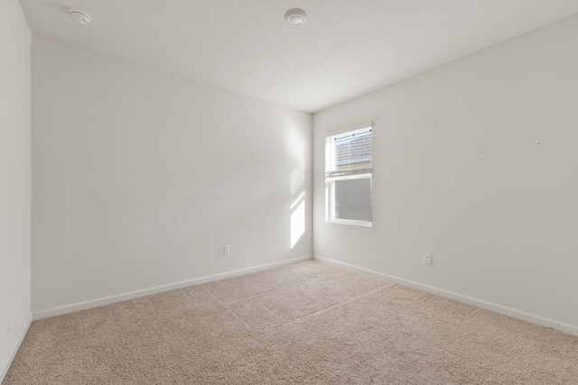 spare room featuring light carpet and baseboards