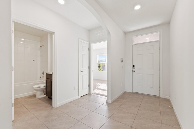 foyer with arched walkways, light tile patterned floors, and baseboards