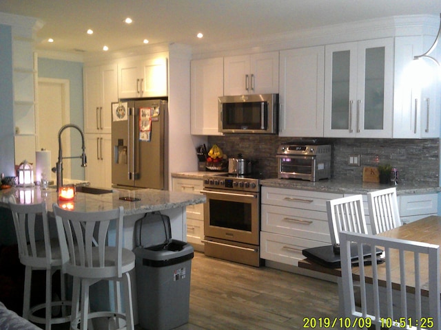 kitchen with light stone countertops, a kitchen breakfast bar, white cabinets, appliances with stainless steel finishes, and decorative backsplash